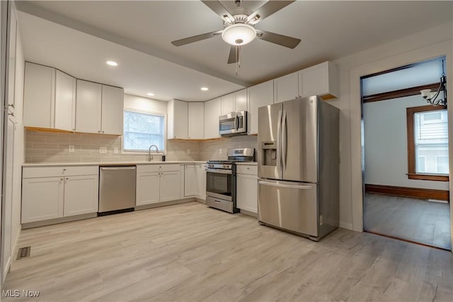kitchen with stainless steel appliances, light wood-type flooring, backsplash, and white cabinetry