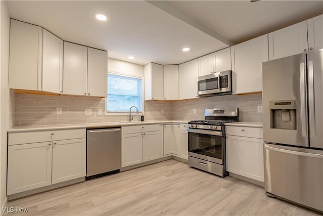 kitchen featuring light wood-type flooring, light countertops, white cabinetry, decorative backsplash, and appliances with stainless steel finishes