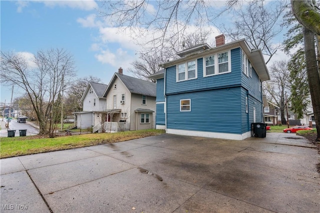 back of property with concrete driveway and a chimney