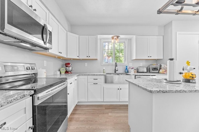 7319 Guilford Rd, Seville, OH 44273 - kitchen featuring light wood-style floors, white cabinets, appliances with stainless steel finishes, light stone counters, and a sink