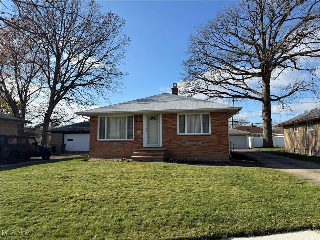 bungalow-style house featuring brick siding, a chimney, a front lawn, and a detached garage