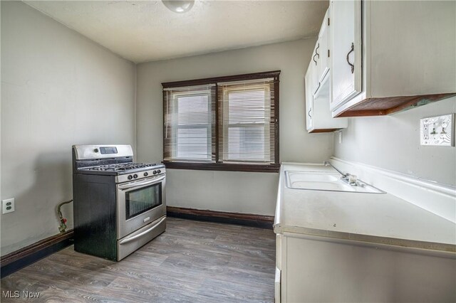 kitchen featuring white cabinets, baseboards, gas range, a sink, and light wood-type flooring
