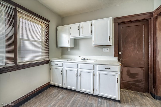 kitchen with baseboards, a sink, light countertops, white cabinetry, and wood finished floors
