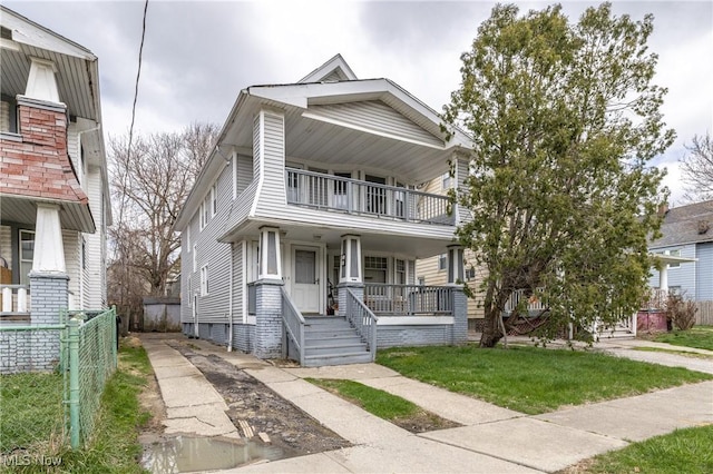american foursquare style home featuring a front yard, a porch, a balcony, and fence
