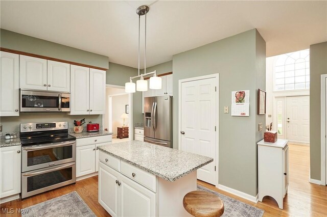 4339 Sierra Dr, Copley, OH 44321 - kitchen featuring hanging light fixtures, appliances with stainless steel finishes, light wood finished floors, white cabinetry, and a kitchen island