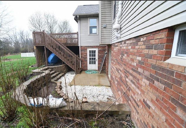 view of home's exterior featuring brick siding, roof with shingles, stairway, and a wooden deck