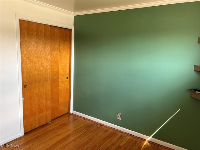 unfurnished bedroom with crown molding, wood finished floors, baseboards, and a closet
