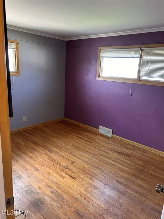 spare room featuring visible vents, hardwood / wood-style flooring, ornamental molding, and a healthy amount of sunlight
