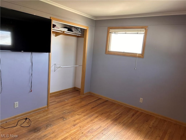 unfurnished bedroom featuring baseboards, light wood finished floors, a closet, and crown molding