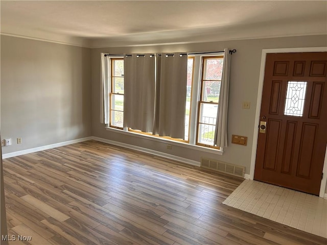 foyer entrance with wood finished floors, baseboards, and visible vents