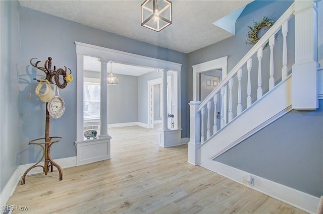 foyer featuring wood finished floors, decorative columns, baseboards, and stairway