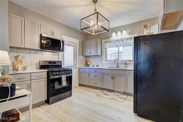 kitchen with freestanding refrigerator, light wood-style flooring, a chandelier, gas stove, and gray cabinetry