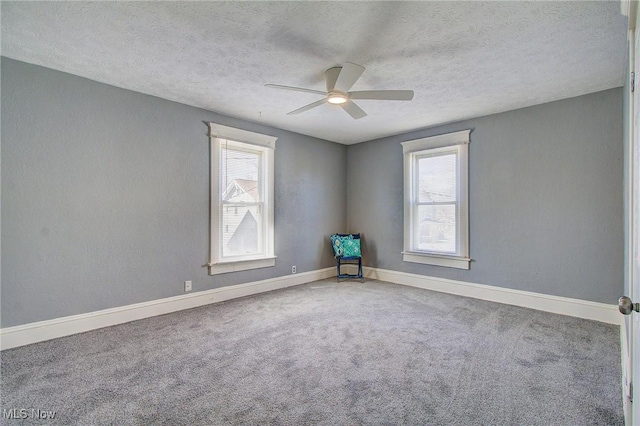 carpeted spare room with a textured ceiling, ceiling fan, baseboards, and a wealth of natural light