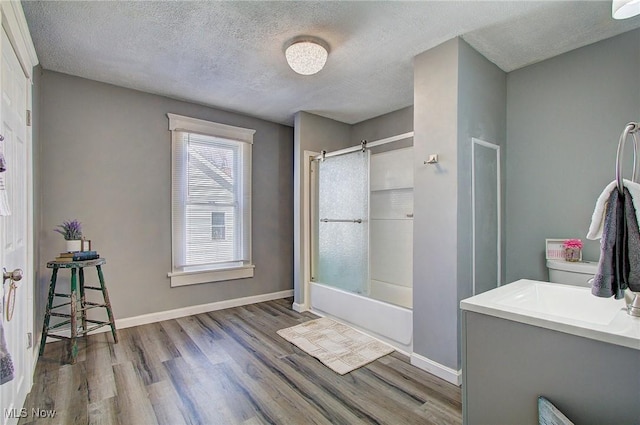 bathroom featuring a textured ceiling, wood finished floors, shower / bath combination with glass door, and baseboards