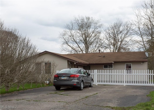 view of side of property featuring aphalt driveway, roof with shingles, and a fenced front yard