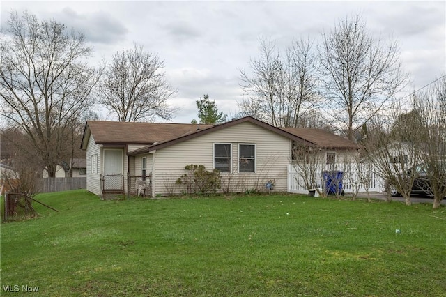 rear view of property featuring fence and a lawn