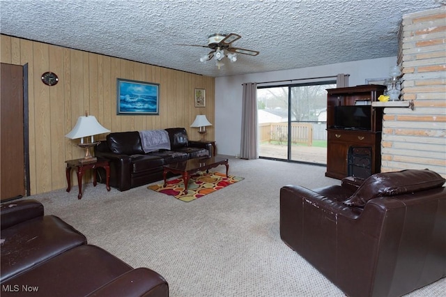 carpeted living area with wood walls, ceiling fan, and a textured ceiling
