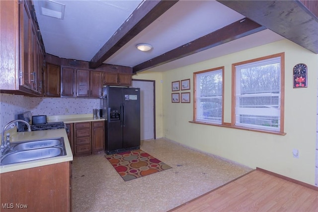 kitchen featuring black fridge with ice dispenser, a sink, light countertops, beamed ceiling, and light wood-style flooring
