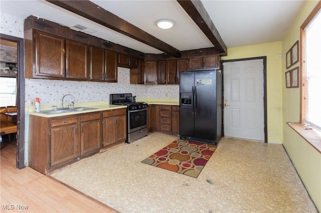 kitchen featuring black fridge with ice dispenser, a sink, light countertops, beam ceiling, and gas stove