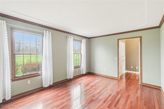 empty room featuring ornamental molding, visible vents, baseboards, and light wood-style floors