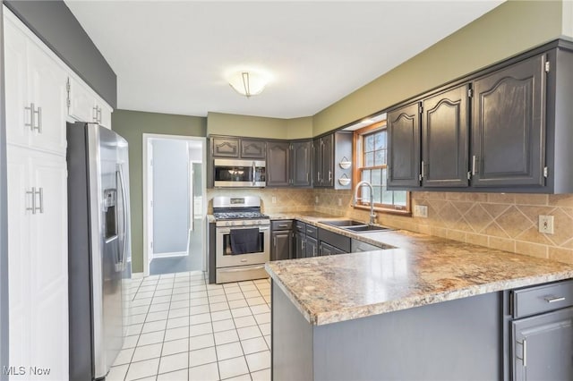 kitchen with light tile patterned floors, tasteful backsplash, a peninsula, appliances with stainless steel finishes, and a sink