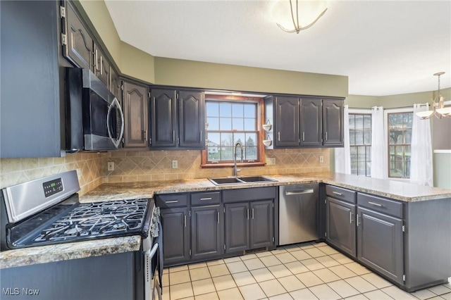 kitchen with tasteful backsplash, a peninsula, appliances with stainless steel finishes, a sink, and a notable chandelier