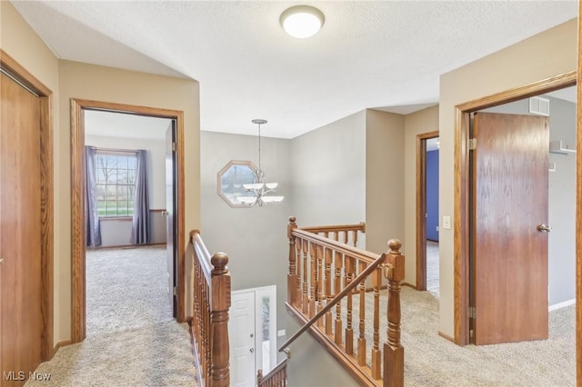 corridor with carpet floors, an upstairs landing, a notable chandelier, and a textured ceiling