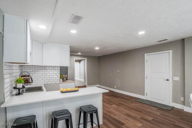 kitchen featuring visible vents, white cabinets, baseboards, a peninsula, and decorative backsplash