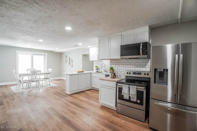 kitchen with a peninsula, a textured ceiling, appliances with stainless steel finishes, light countertops, and a sink