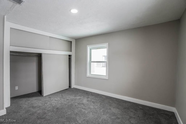 unfurnished bedroom with dark colored carpet, visible vents, a closet, and a textured ceiling