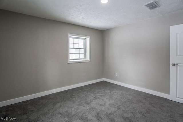 spare room featuring dark carpet, baseboards, visible vents, and a textured ceiling