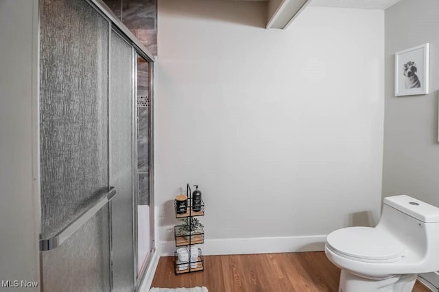 bathroom featuring toilet, a shower stall, wood finished floors, and baseboards