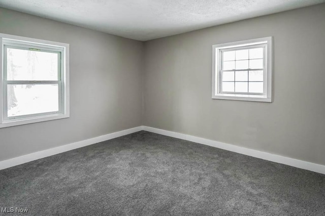 spare room with dark carpet, a textured ceiling, and baseboards