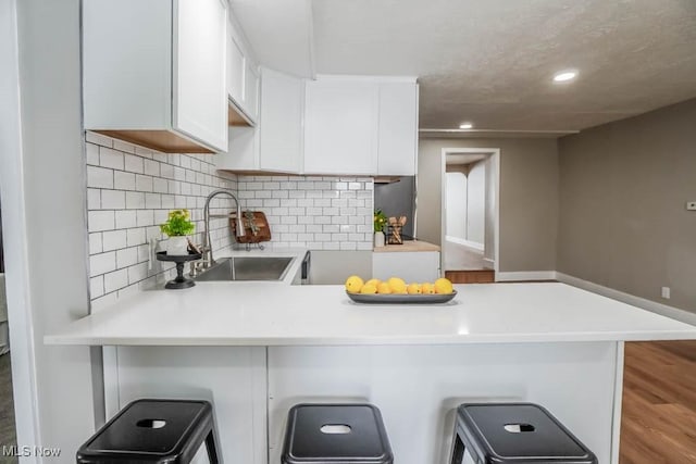 kitchen with light countertops, a peninsula, a sink, and white cabinets