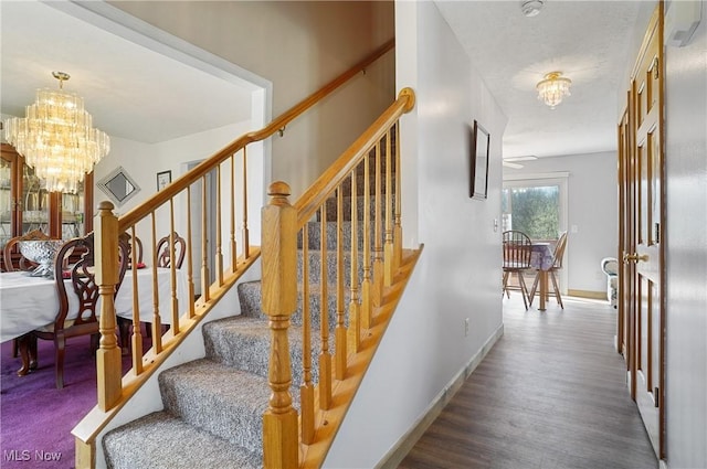 stairway featuring wood finished floors, a notable chandelier, and baseboards