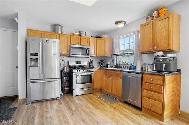 kitchen featuring a sink, dark countertops, light wood finished floors, and stainless steel appliances
