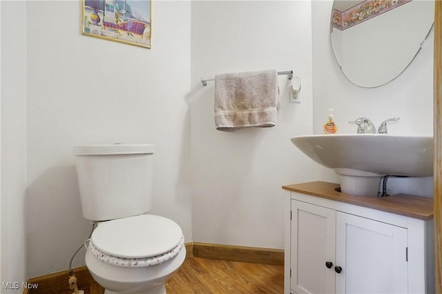half bath with baseboards, a sink, toilet, and wood finished floors