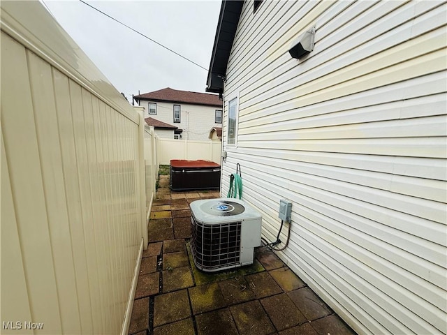 view of side of home with a patio, fence, a hot tub, and central AC unit