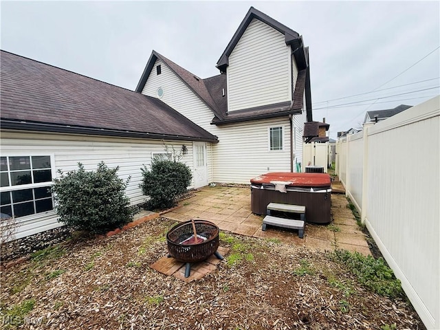 rear view of property with a fenced backyard, a fire pit, a hot tub, a patio, and roof with shingles