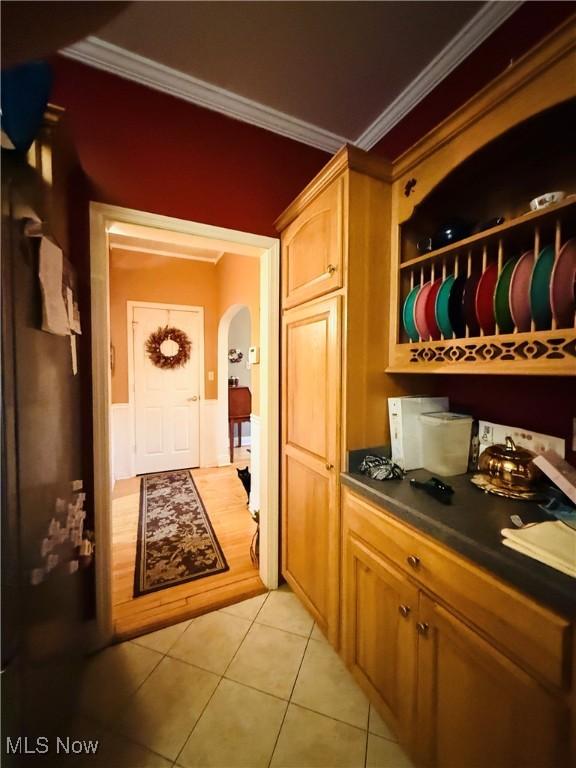 hallway with light tile patterned floors, crown molding, and arched walkways