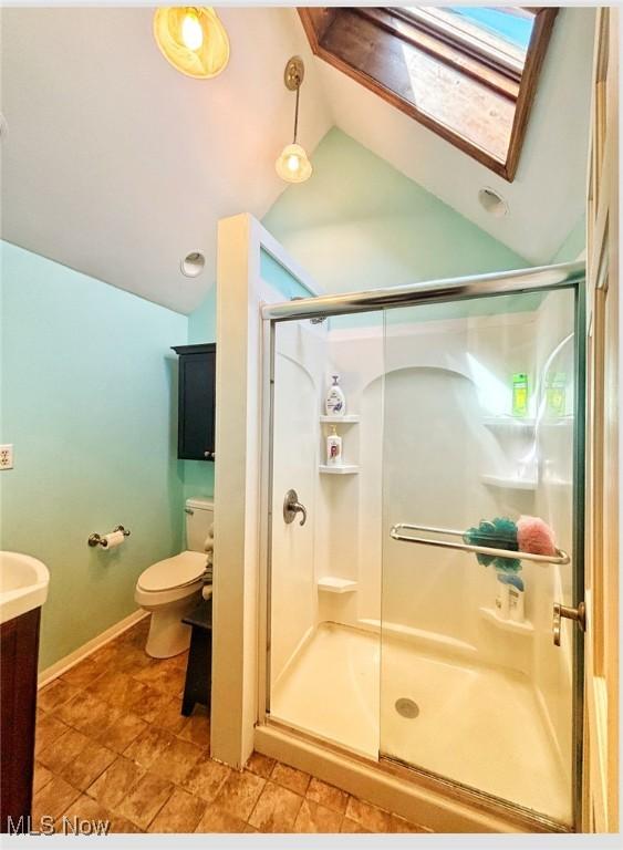 bathroom with vaulted ceiling with skylight, vanity, toilet, a stall shower, and baseboards