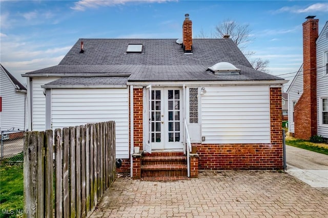 rear view of house featuring a chimney, french doors, entry steps, fence, and a shingled roof
