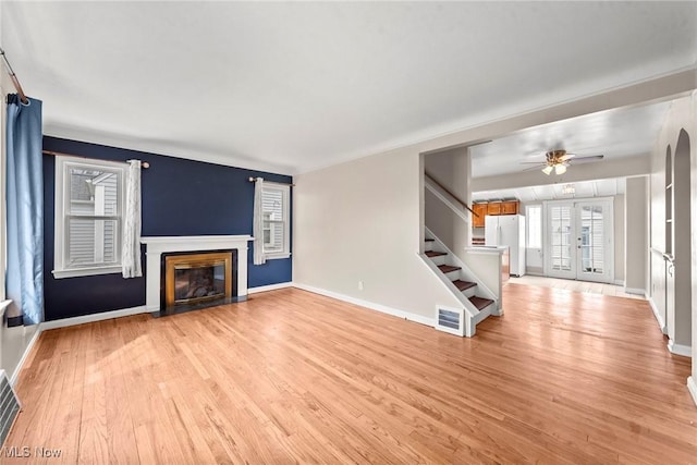 unfurnished living room featuring light wood-type flooring, baseboards, stairway, a fireplace with flush hearth, and visible vents