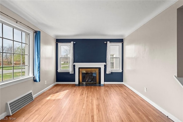 unfurnished living room with light wood-style flooring, a glass covered fireplace, visible vents, and a wealth of natural light