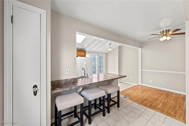 kitchen featuring a kitchen breakfast bar, freestanding refrigerator, dark countertops, brown cabinetry, and ceiling fan