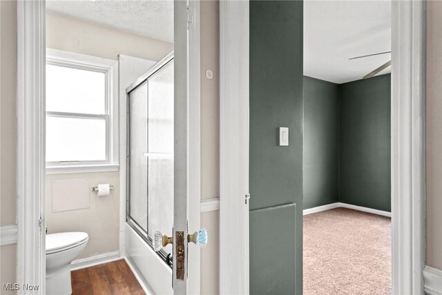 full bathroom with combined bath / shower with glass door, baseboards, and toilet