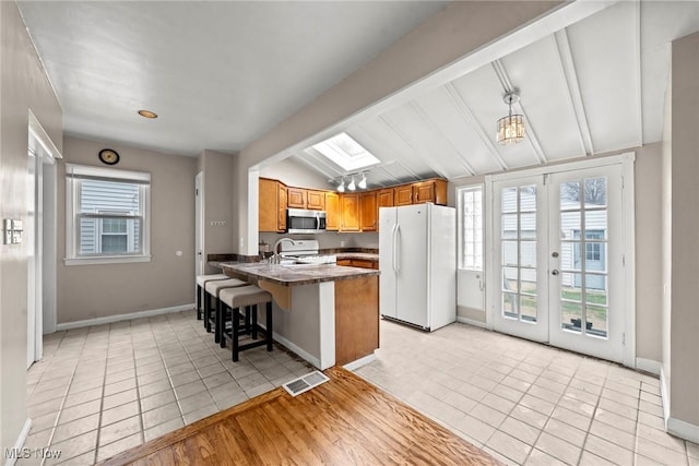 kitchen with visible vents, vaulted ceiling with skylight, light tile patterned floors, white appliances, and a peninsula
