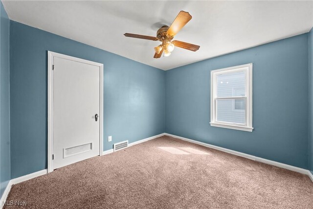 carpeted spare room with visible vents, baseboards, and a ceiling fan