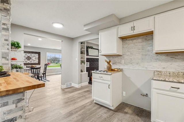 kitchen featuring light stone countertops, light wood-style flooring, tasteful backsplash, visible vents, and white cabinets