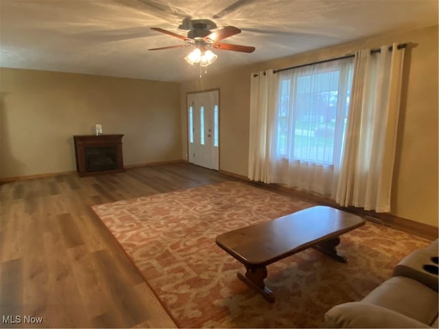 unfurnished living room with baseboards, a ceiling fan, wood finished floors, and a fireplace